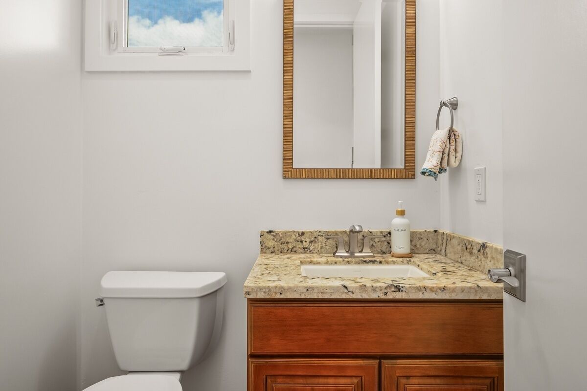 A bathroom with a toilet, a sink with a granite countertop, a wooden vanity, a mirror with a gold frame, and a towel hanging on a towel rack.