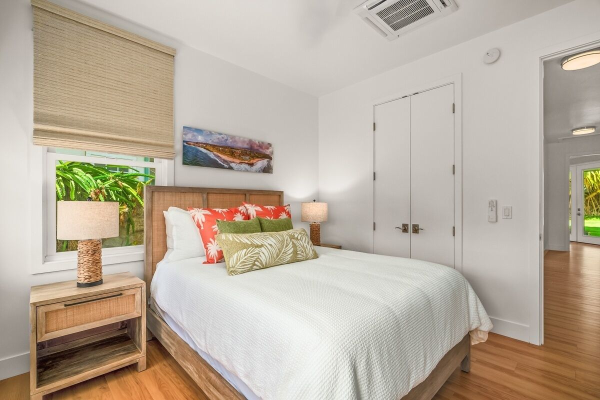 Un dormitorio con una cama, mesitas de noche, una ventana con persianas, un cuadro y una puerta.