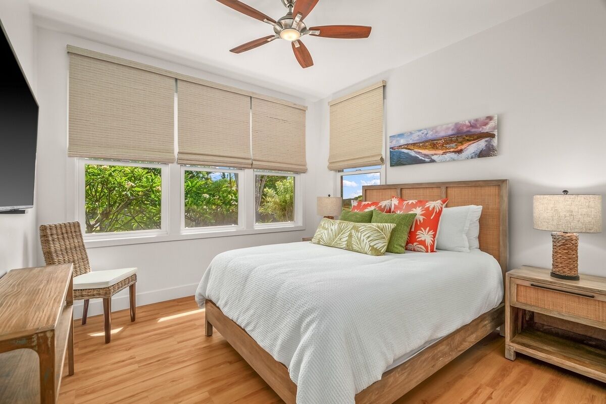 A bedroom with a bed, a ceiling fan, a nightstand, a chair, and large windows with blinds.