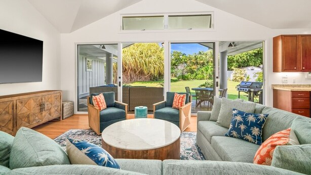 A modern living room with a sectional sofa, a coffee table, and a dining area with chairs. - Kauai 2247 Loke Road 3 Bedroom Home (Koloa)