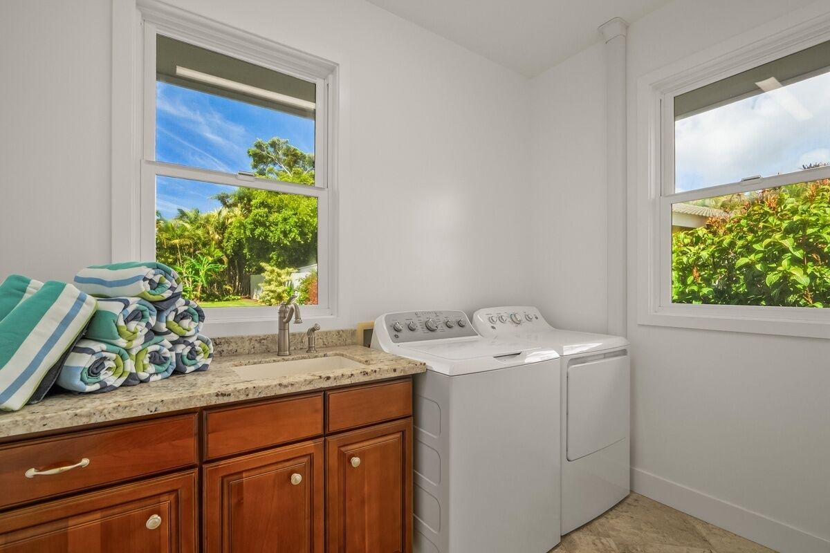A laundry room with a washing machine, a sink, and a window with a view of greenery.