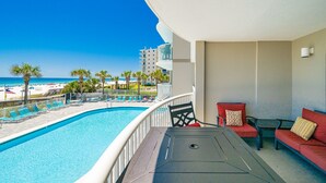 A balcony with a pool, red seating, and a view of the beach and ocean. - Tradewinds 102 1 Bedroom Condo (Orange Beach)