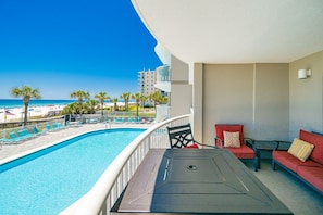 A balcony with a pool, red seating, and a view of the beach and ocean. - Tradewinds 102 1 Bedroom Condo (Orange Beach)
