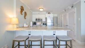 A kitchen with a marble countertop, stainless steel appliances, and a bar stool seating area. - Tradewinds 102 1 Bedroom Condo (Orange Beach)