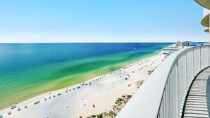 Vista a la playa desde un balcón, cielo despejado, arena y algunas sombrillas.