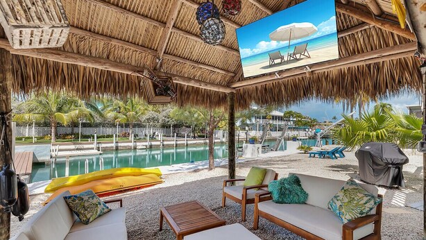 Un área de estar al aire libre techada con piscina, sillones de descanso y un mural con una playa.