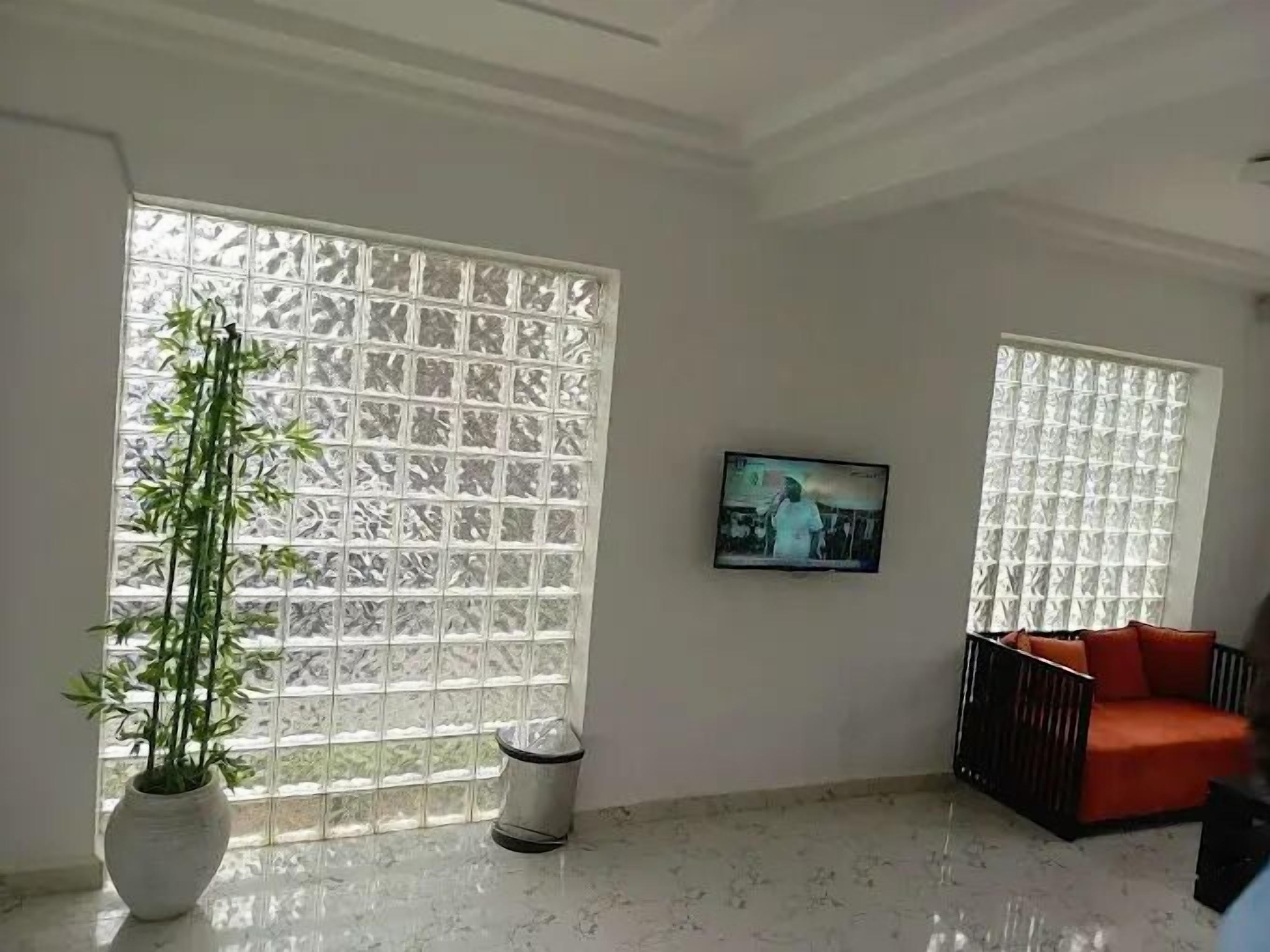 Una habitación con un ventanal grande, una planta en maceta, un televisor en la pared y un sofá rojo.