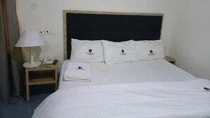 Ett hotellrum med en säng, ett nattduksbord, en lampa, en telefon och en luftkonditioneringsanläggning.