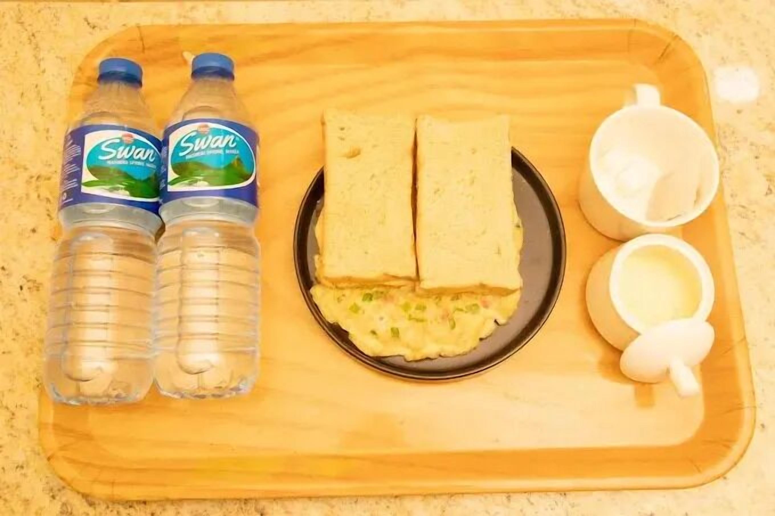 A tray with two bottles of Swan water, two sandwiches, a plate with a spread, and two white cups.
