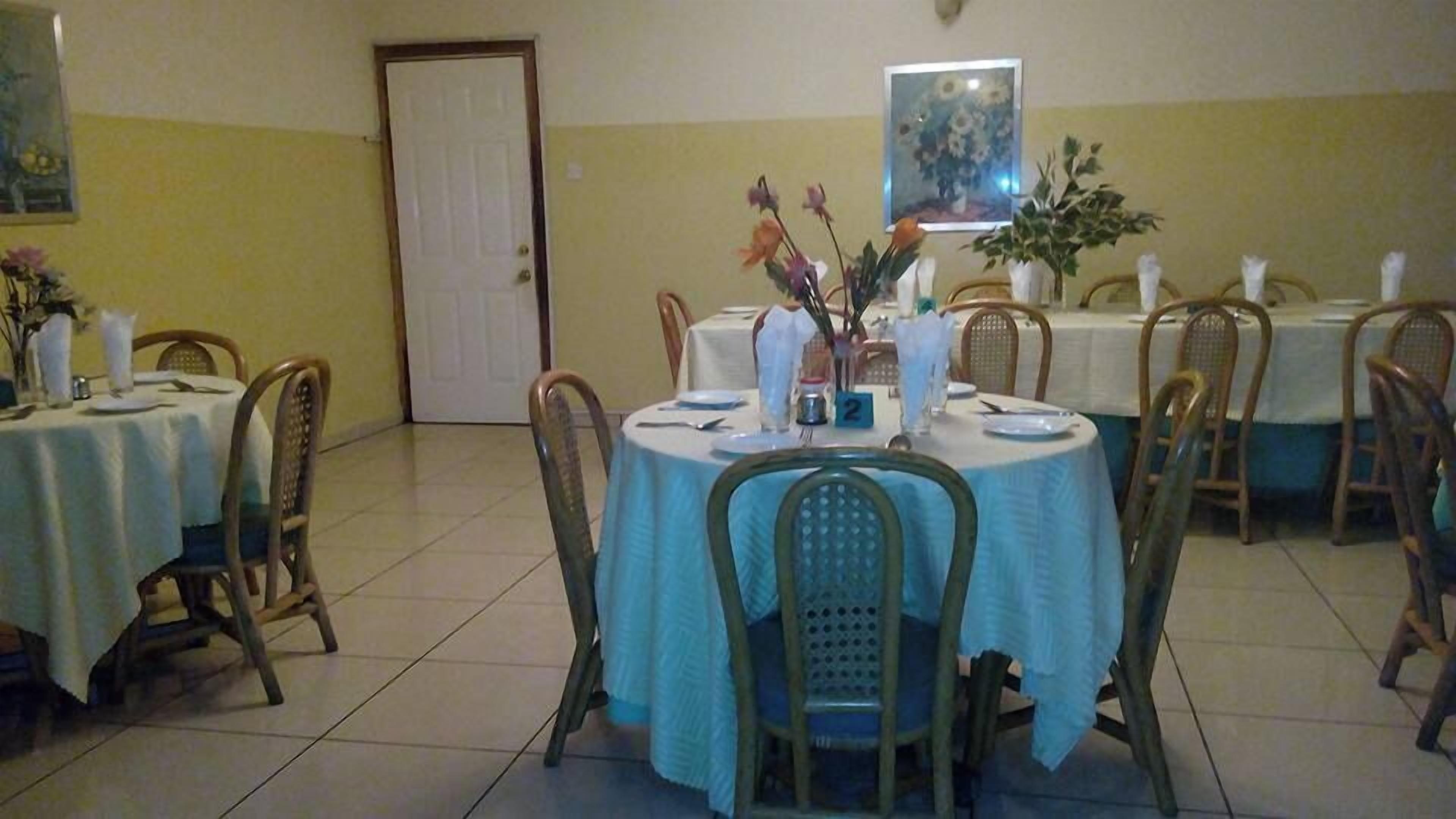 A dining area with round tables covered in white tablecloths, wooden chairs, and floral centerpieces.