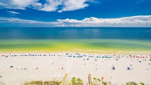 Ein Strand mit vielen Sonnenschirmen und Liegestühlen, einer Holzpromenade und freiem Blick auf das Meer.