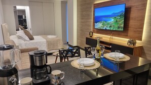 Un salon moderne doté d’un grand téléviseur, d’un coin repas avec un bar et d’un espace salon confortable.