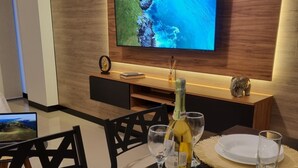 Un espace repas moderne avec un téléviseur fixé à un mur en bois, une bouteille de champagne et un verre sur la table.
