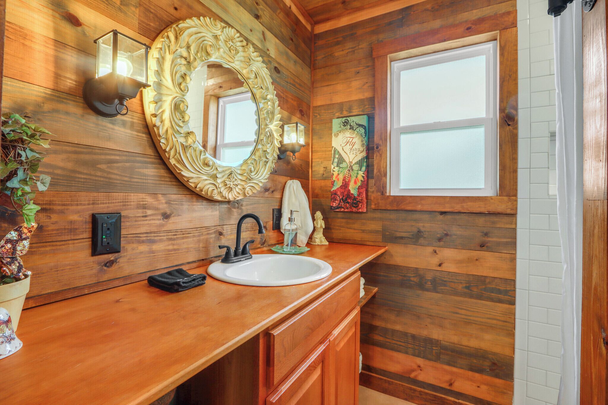 A wooden bathroom with a white sink, a decorative mirror, and a wall-mounted light fixture.