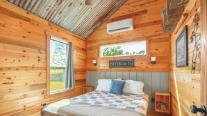 A cozy wooden cabin bedroom with a bed, a window, a wall-mounted air conditioner, and a motivational sign.