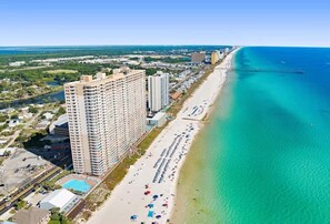 A high-rise hotel with multiple floors, a beach with umbrellas, and a clear blue ocean. - Skywaves Escape 2503-Stunning Views-Sleeps 5 (Panama City Beach)