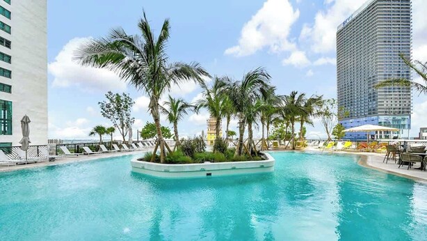 A pool area with palm trees, lounge chairs, and a view of a tall building.