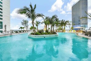 A pool area with palm trees, lounge chairs, and a view of a tall building. - 39th Floor 2BR  Bay View Downtown Miami Sleeps 6 (Miami)