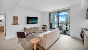 A modern apartment with a large balcony, a city view, a dining area, and a living room with a sofa and chairs.