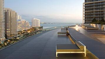 A rooftop terrace with a view of the ocean, featuring sun loungers and a railing.