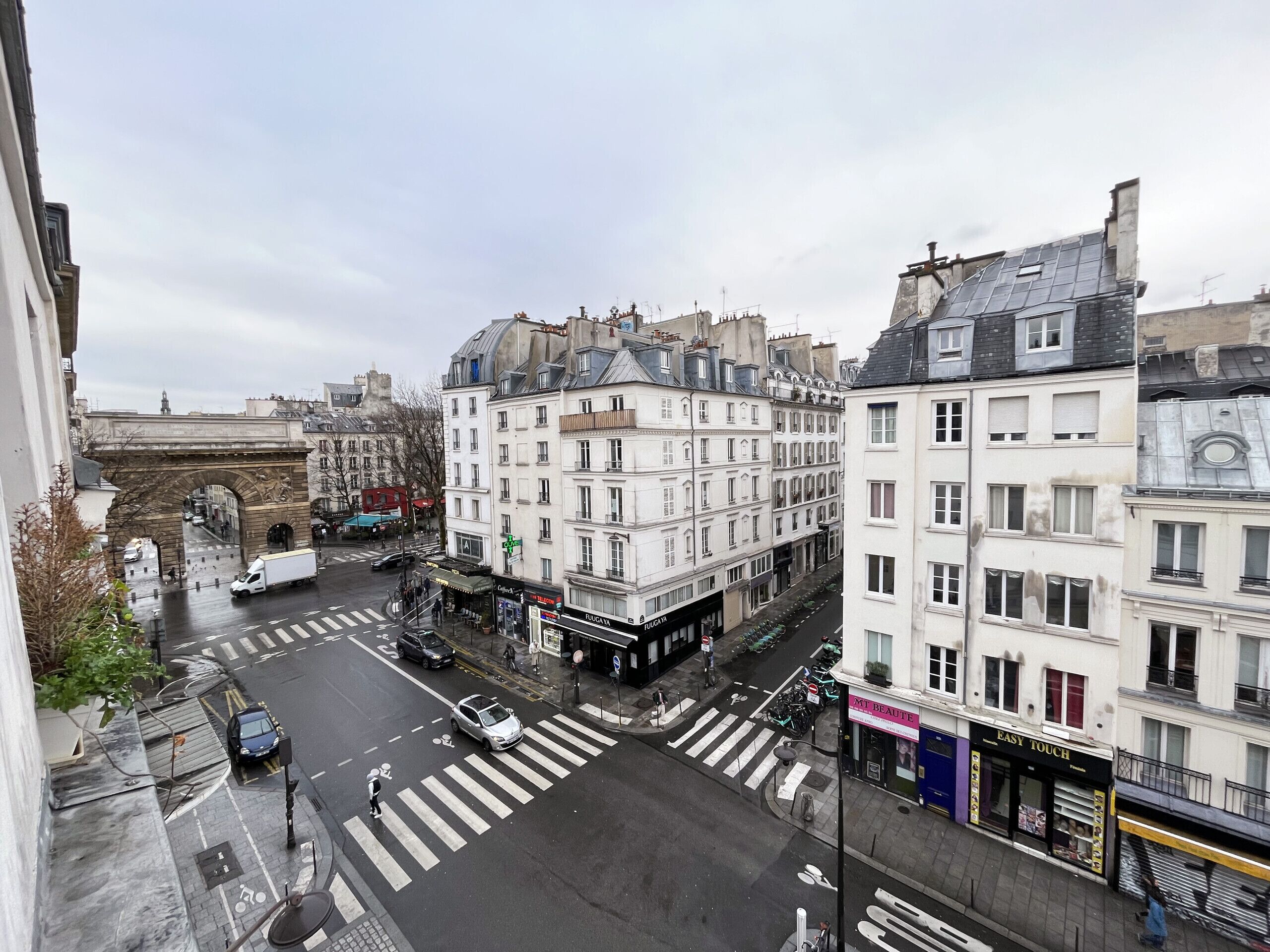 A street view with a pedestrian crossing, buildings with commercial establishments, and a historic archway.