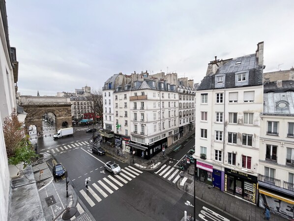 A street view with a pedestrian crossing, buildings with commercial establishments, and a historic archway.