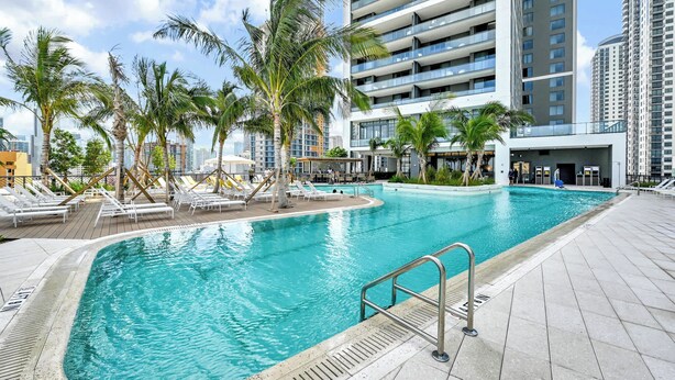 A swimming pool with lounge chairs and palm trees, surrounded by high-rise buildings. - Corner 2BR · 42nd Floor Bay & City Views Sleeps 6 (Miami)