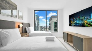 Una habitación de hotel moderna con dos camas, un ventanal con vistas a la ciudad, un televisor de pantalla plana y una consola de madera.