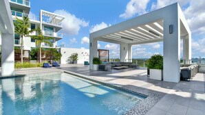 A modern rooftop pool area with a clear blue pool, outdoor seating, and a view of the city skyline. - Design District Studio · City View · Free Parking (Miami)
