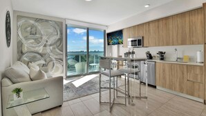 A modern kitchen with a large window, a dining area with a glass table, and a sofa with a plant. - Design District Studio · City View · Free Parking (Miami)