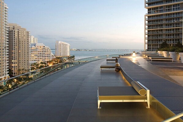 A rooftop terrace with seating areas, a glass railing, and a view of the cityscape and water.