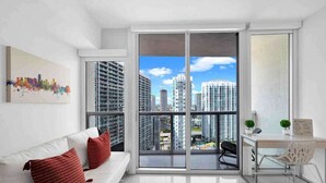 A modern apartment with a white sofa, red cushions, a desk, and a large sliding glass door to a city view. - Icon Brickell Studio  City View Pool & Spa (Miami)
