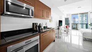 A modern kitchen with stainless steel appliances, wooden cabinets, and a dining area with a glass table and chairs. - Icon Brickell Studio  City View Pool & Spa (Miami)