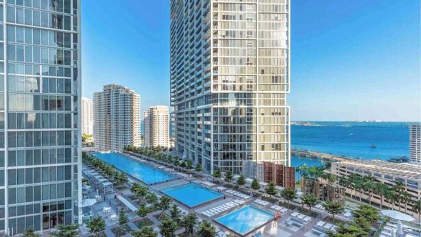 A high-rise building with a glass facade, a pool area with multiple pools, and a view of the sea. - Icon Brickell Studio  City View Pool & Spa (Miami)