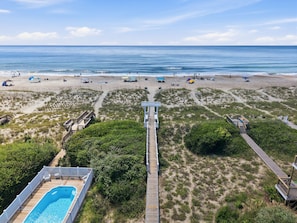 A beach with a wooden boardwalk leading to a pool area, surrounded by dunes and beach umbrellas. - Emerald Sunsets: Pet-Friendly Beach Home (Emerald Isle)
