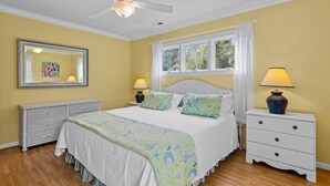Ein Schlafzimmer mit einem Bett, Nachttischen, einer Kommode, einem Deckenventilator und einem Fenster mit Vorhängen.