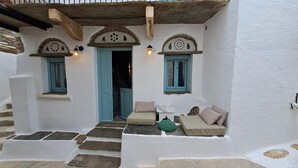 Un edificio tradicional blanco con puertas y ventanas azules, escalones de piedra que conducen a un área de descanso con cojines.