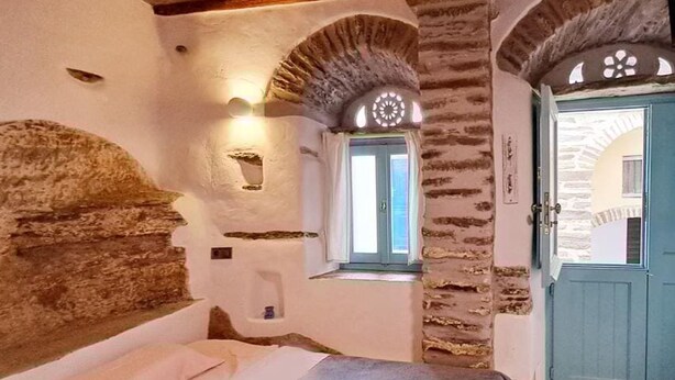 Una habitación con paredes de piedra a la vista, una cama, un ventanal con vistas y una puerta azul.