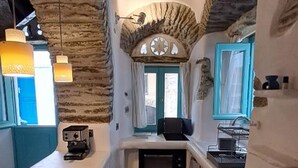 Una cocina compacta con un arco de piedra, un pequeño comedor y un ventanal con cortinas.