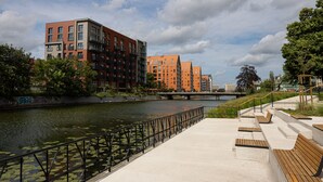 A riverside walkway with benches and a railing, alongside modern buildings and a bridge. - Apartament Terra r Dmie cie nad sam Mot aw (Gdańsk)