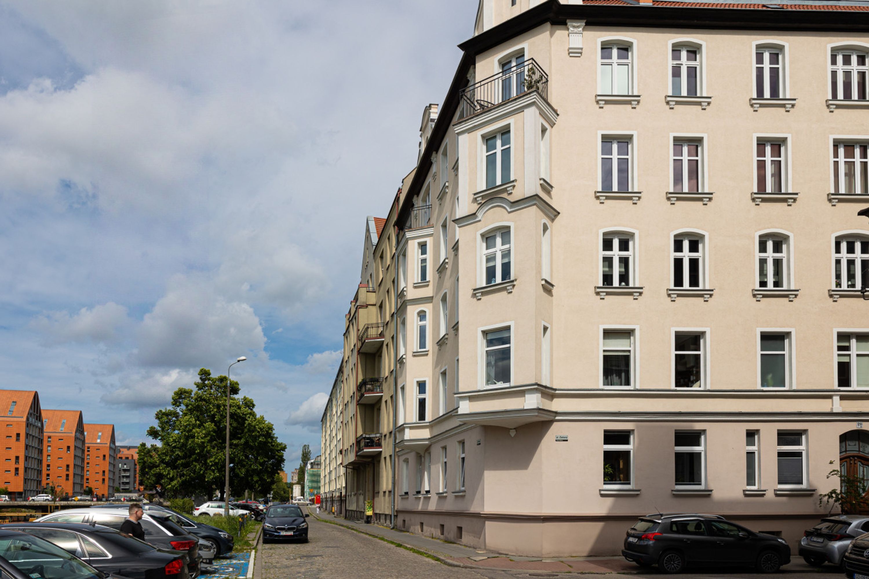 A multi-story building with a row of windows on the ground floor, parked cars along the street, and a clear sky.