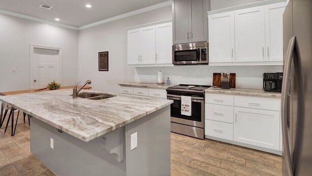 Una cocina moderna con armarios blancos, un refrigerador de acero inoxidable, un horno empotrado y una isla con encimera de granito.