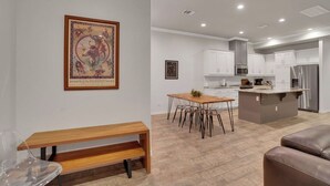 Una cocina moderna con armarios blancos, una isla central y un comedor con mesa y sillas de madera.