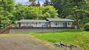 A two-story cabin with a deck, surrounded by dense forest. - Zenith at Copalis Rocks - Unsurpassed Ocean View with new Hot Tub (Copalis Beach)