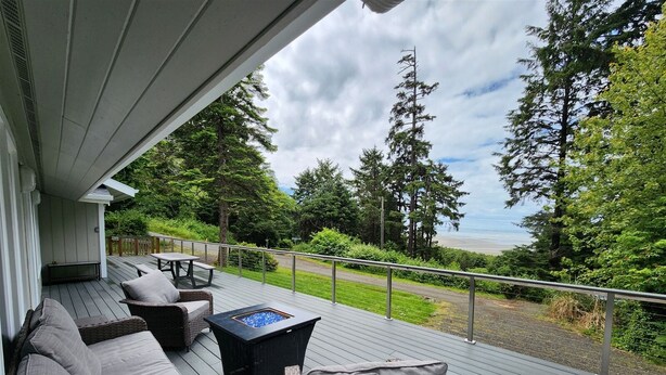 A covered deck with wicker furniture and a fire pit, overlooking a beach and forested area. - Zenith at Copalis Rocks - Unsurpassed Ocean View with new Hot Tub (Copalis Beach)