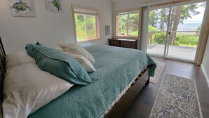 A bedroom with a bed, pillows, a nightstand, a window, and a view of the outdoors. - Zenith at Copalis Rocks - Unsurpassed Ocean View with new Hot Tub (Copalis Beach)