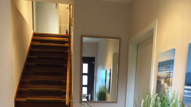 A modern interior with a wooden staircase, a glass-fronted cabinet, and a mirror reflecting a door and a painting. - Charming apartment, ideal for longer stays and families (Kiel)