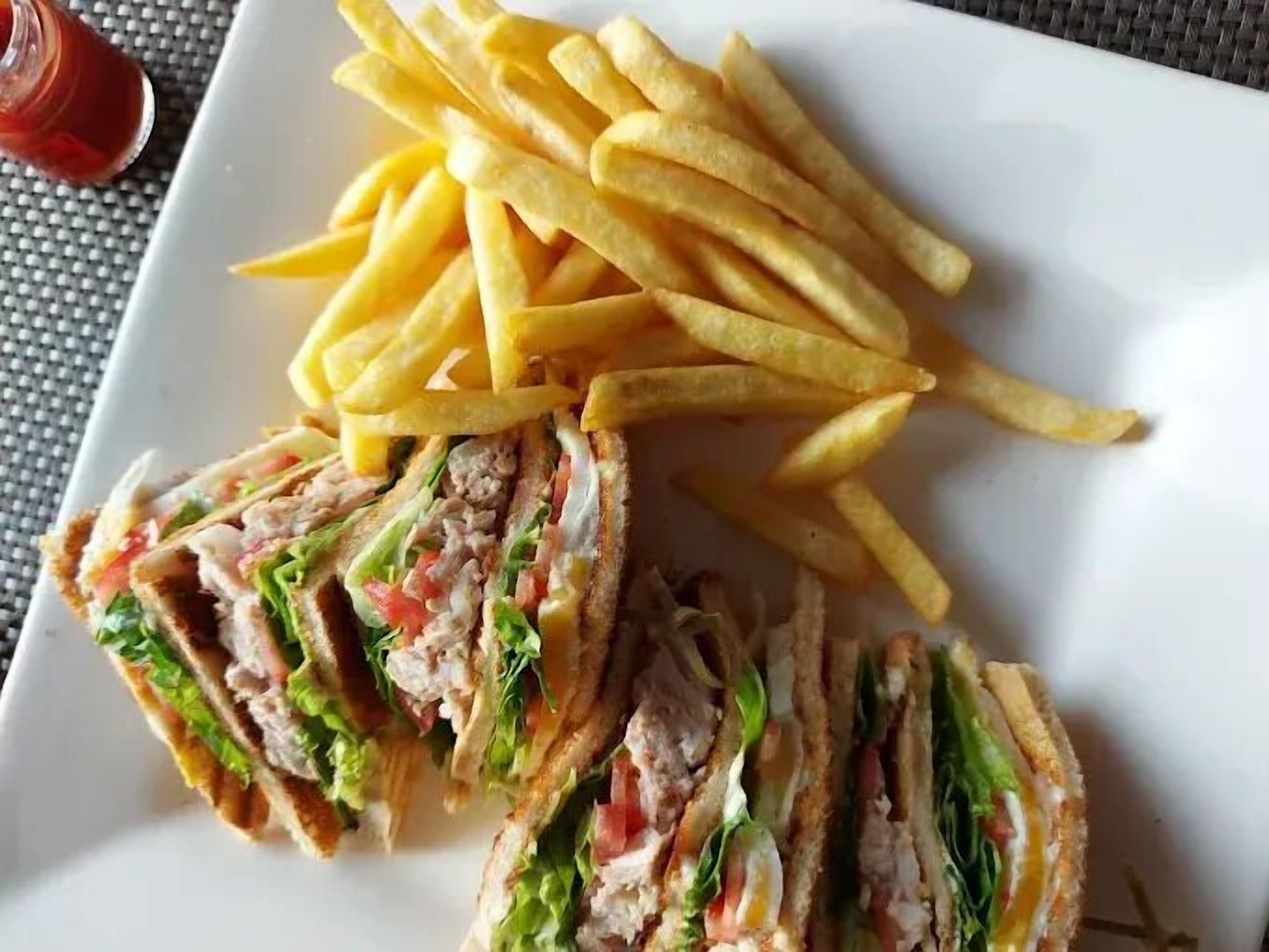 A sandwich cut in half with lettuce, tomato, and meat, served with a side of French fries on a white plate.