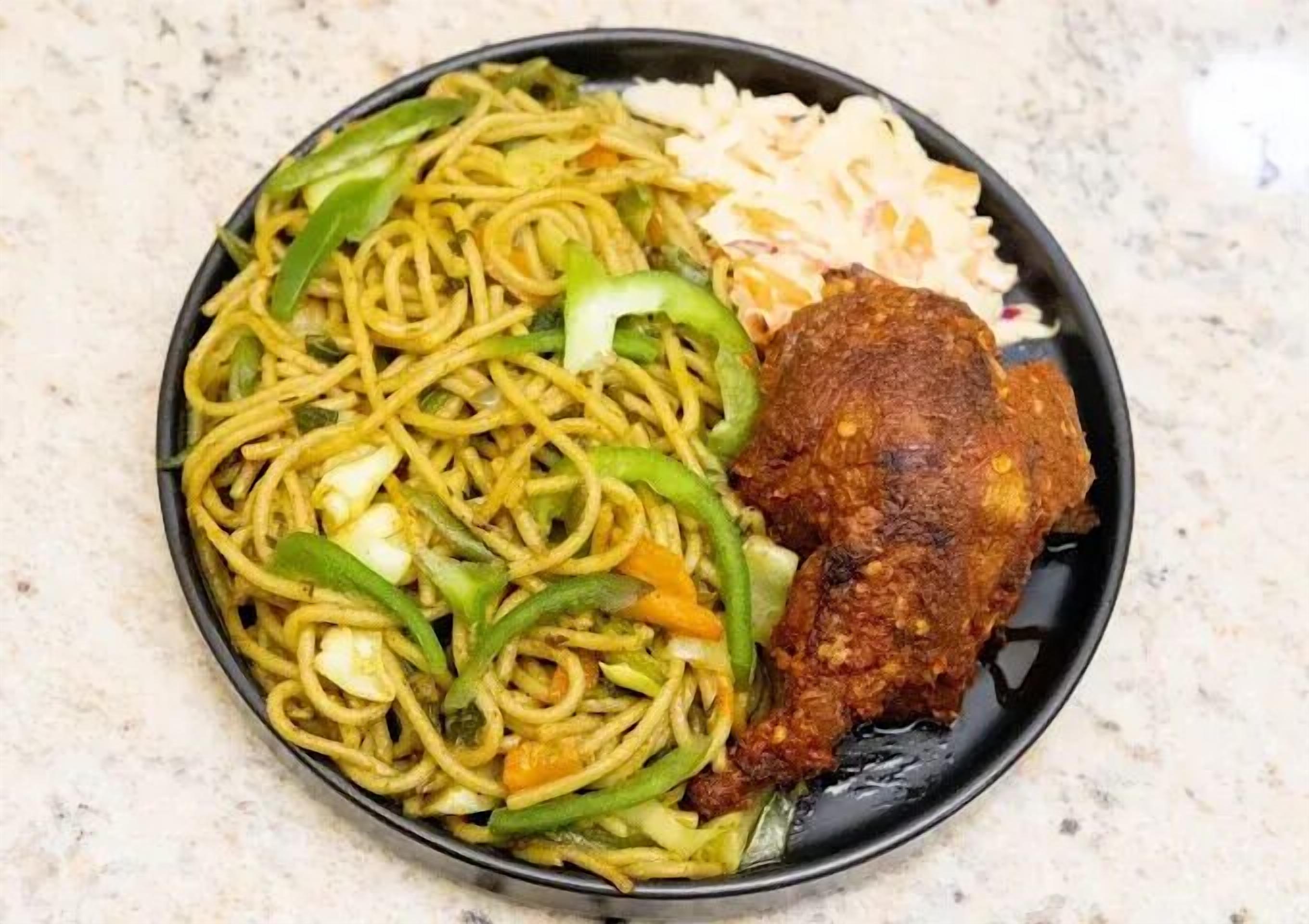 A plate of noodles with vegetables and a fried chicken piece.