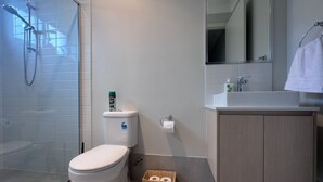 Un baño moderno con inodoro, bidé y ducha. Hay un cesto con papel higiénico y un perchero para toallas.